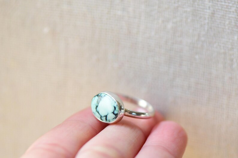May include: A silver ring with a light blue and white oval gemstone. The ring is set in a simple band.