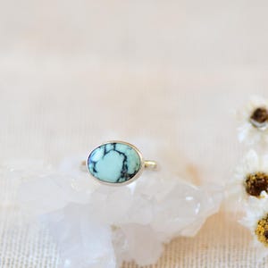 May include: A silver ring with a light blue oval turquoise stone set in the center. The stone has black veins running through it.