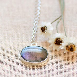 Op de afbeelding: Een zilveren ketting met een ronde hanger met een iriserende labradorit-edelsteen.