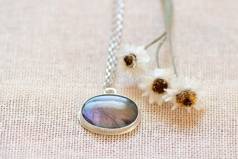 Op de afbeelding: Een zilveren ketting met een ronde hanger met een iriserende labradorit-edelsteen.