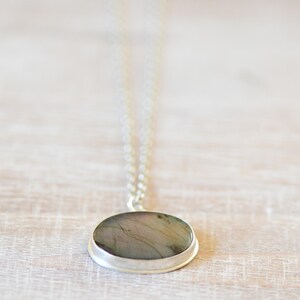 Op de afbeelding: Een zilveren ketting met een ronde hanger met een grijze en groene steen.