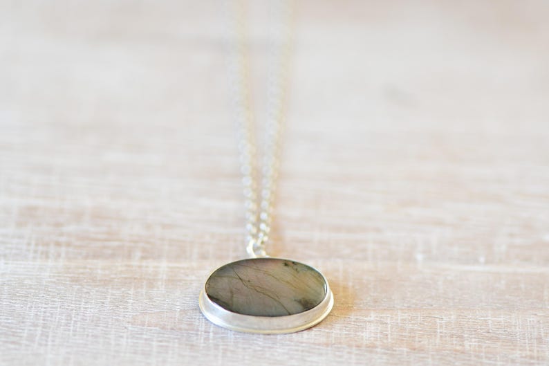 Op de afbeelding: Een zilveren ketting met een ronde hanger met een grijze en groene steen.