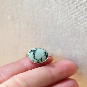May include: A silver ring with a light blue oval turquoise stone set in the center.