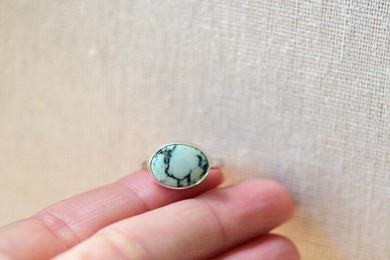 May include: A silver ring with a light blue oval turquoise stone set in the center.
