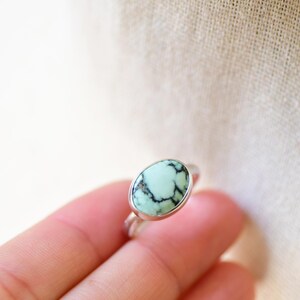 May include: A silver ring with a light green oval turquoise stone set in a bezel setting.