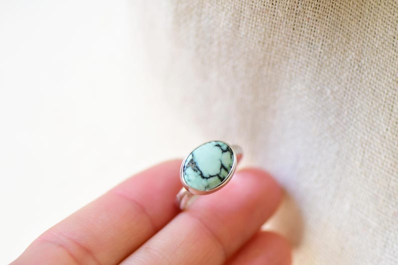 May include: A silver ring with a light green oval turquoise stone set in a bezel setting.