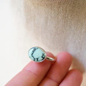 May include: A silver ring with a light blue oval turquoise stone set in the center. The stone has black veins running through it.