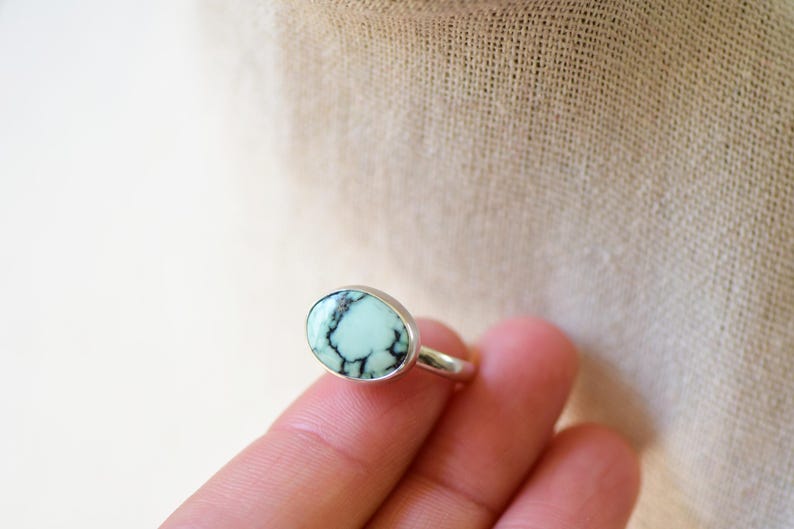 May include: A silver ring with a light blue oval turquoise stone set in the center. The stone has black veins running through it.