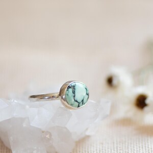May include: A silver ring with a round, green and black turquoise stone.