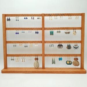 May include: A wooden earring display stand with multiple rows of holes to hold various earrings. The stand is made of light brown wood and is filled with a variety of earrings in different styles and colors, including studs, hoops, and dangles.