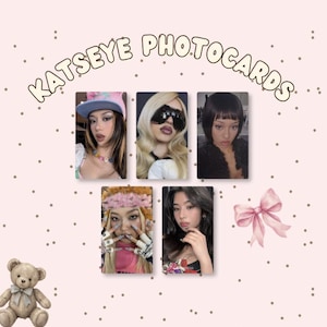 May include: A collection of five rectangular Katseye photocards displayed on a light pink background with scattered dots, a small brown teddy bear, and a pink bow. The text KATSEYE PHOTOCARDS is printed in a curved, light-colored font above the cards.