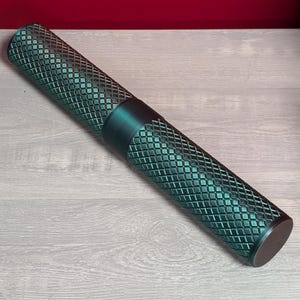 May include: A teal-coloured metal roller with a diamond-shaped pattern. The roller is on a light grey wooden surface.