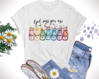 May include: White t-shirt with the text "God says you are" and a row of colorful jars with flowers and butterflies. The jars are labeled with words like "Unique", "Special", "Lovely", "Precious", "Strong", "Chosen", and "Forgiven".