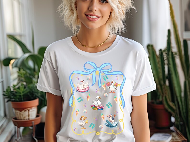 May include: White t-shirt with a blue ribbon and a graphic of ducks enjoying summer activities, including ice cream cones, flip flops, and a surfboard.