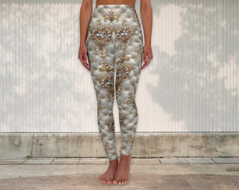 Puede incluir: Leggings de cintura alta con un patrón acolchado en tonos blancos y dorados. Los leggings presentan diseños de filigrana dorada ornamentados con acentos brillantes. El diseño general se asemeja a una estética vintage lujosa. Los leggings son ajustados y llegan a los tobillos.