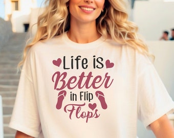 Könnte beinhalten: Weißes T-Shirt mit einer pinkfarbenen Grafik, auf der "Life is Better in Flip Flops" mit zwei pinkfarbenen Herzen und einem Paar pinkfarbener Flip-Flops steht.