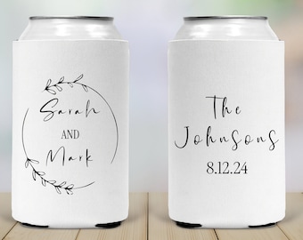 May include: Two white can coolers with black text. The first cooler has a floral wreath with the text "Sarah and Mark". The second cooler has the text "The Johnsons 8.12.24".
