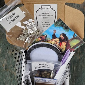 May include: A craft kit in a cardboard box containing bags of 8mm and 10mm beads, a crucifix and center charm set, a spool of 0.90 mm nylon cord, a circular foam pad, and a religious card depicting a scene with figures in a landscape setting.