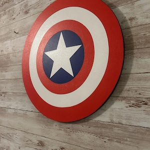 May include: A red, white, and blue Captain America shield with a white star in the center. The shield is made of wood and has a black border.
