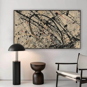 Pu&ograve; includere: Un dipinto astratto in bianco e nero con schizzi di rosso e giallo su uno sfondo beige. Il dipinto &egrave; incorniciato in nero e appeso a una parete bianca. Una lampada nera con un paralume a cupola e un tavolino in legno scuro sono in primo piano.