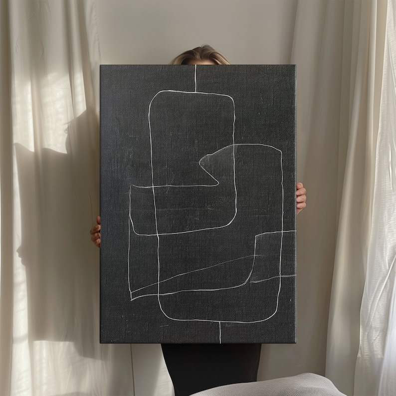 May include: A black canvas with white abstract lines drawn on it. The canvas is being held by a person.