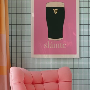 May include: A pink poster with a black and white illustration of a pint of Guinness. The poster has the word "sl&aacute;inte" written in white at the bottom.