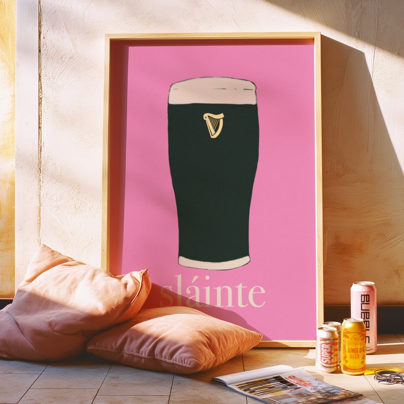 May include: A pink framed poster with a black and white illustration of a pint of Guinness. The poster says "sl&aacute;inte" in white text.