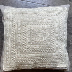 May include: A white throw pillow with a square embroidered design. The embroidery is a series of concentric squares with different stitch patterns.