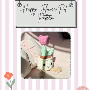 May include: A crocheted flower pot with a smiling face, a pink flower, and green leaves. The flower pot is white with a brown rim. The text "Happy Flower Pot Pattern" is above the flower pot.