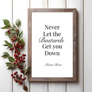 以下が含まれることがあります： 白い背景に黒い文字で「Never Let the Bastards Get you Down」と書いてある額装されたプリント。モイラ・ローズによる作品です。
