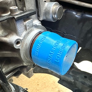 May include: A bright blue 3D-printed camshaft oil seal for Subaru engines. The text "SUBARU" and "CAMSHAFT OIL FOR 305" is printed on the side of the seal. The seal is installed on a metal engine component.
