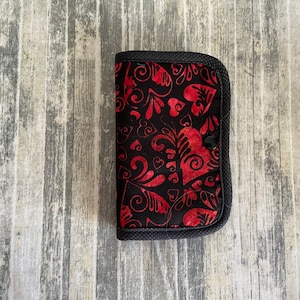 May include: A black fabric wallet with a red and black heart pattern. The wallet has a snap closure.