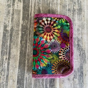 May include: A small, colourful fabric pouch with a pink zipper and a purple button. The pouch is decorated with a floral pattern.
