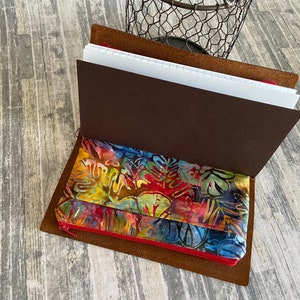May include: A brown leather journal with a zippered pocket. The pocket is lined with a colorful fabric with a floral pattern. The journal is open to reveal blank pages.