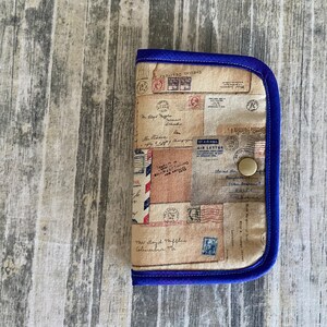 May include: A small, rectangular pouch with a blue trim and a vintage-style fabric featuring a pattern of old letters and stamps. The pouch has a single button closure.