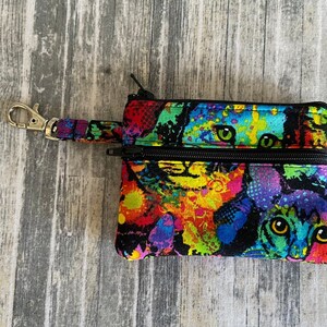 May include: A small black zippered pouch with a colorful cat print. The pouch has a silver key ring attached.