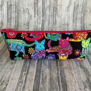 May include: A black zippered pouch with a colorful print of cats and flowers. The cats are in various poses and have bright colors and patterns.