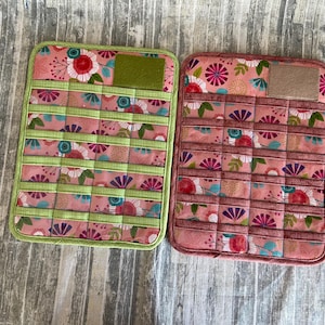 May include: Two fabric storage organizers with a floral pattern and multiple compartments. The organizer on the left has a green border and the organizer on the right has a red border.