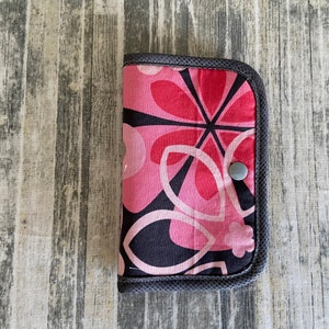 May include: A pink and black floral patterned zippered pouch with a gray button.