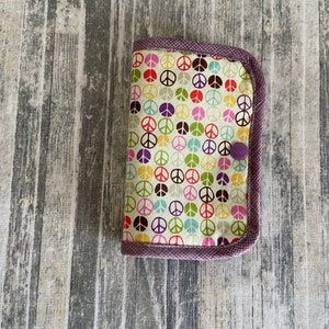 May include: A small purple fabric wallet with a peace sign pattern. The wallet has a purple button closure.