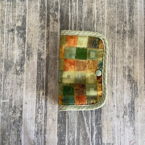 May include: A small green fabric wallet with a geometric pattern in shades of brown, orange, and green. The wallet has a button closure.