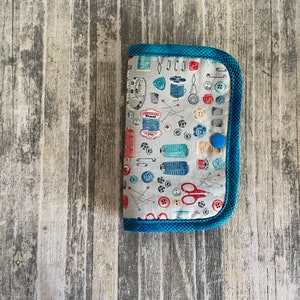 May include: A blue and white fabric sewing kit with a blue button closure. The fabric features a pattern of sewing supplies, including needles, thread, buttons, and scissors.