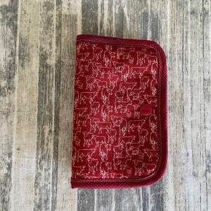 May include: A red fabric pouch with a white cow print design and a single button closure.
