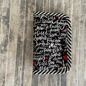 Peut inclure: Pochette en tissu rayée noir et blanc avec un fond noir et des mots français blancs et des cœurs rouges. Les mots incluent "Salut!", "Bonjour", "Je t'aime", "Amour", "Oui", "Bisous", "Lamour", "Paris", "Oh la la", "Bon Voyage", et plus.