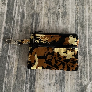 May include: A small black zippered pouch with a brown and cream floral print. The pouch has a silver metal clip attached to it.