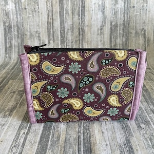 May include: A small purple and brown paisley patterned zippered pouch with a light purple trim.