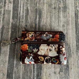 May include: A brown zippered pouch with a dog print design. The pouch has a metal clasp and two zippers. The print features various breeds of dogs, including a golden retriever, a pug, and a shih tzu.