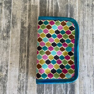 May include: A small, teal blue zippered pouch with a colourful geometric pattern. The pouch has a single teal blue button.