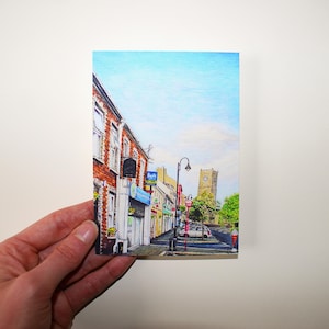 Peut inclure: Une illustration colorée d'une scène de rue dans une ville. La rue est bordée de bâtiments en briques avec des magasins et des entreprises. Il y a une tour d'horloge au loin. Le ciel est bleu avec des nuages blancs.