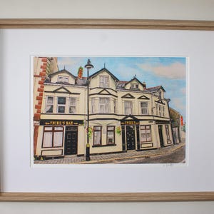 Peut inclure: Une peinture à l'aquarelle d'un bâtiment jaune avec des bordures et des fenêtres noires. Le bâtiment porte une enseigne qui indique "The Friel's Bar".